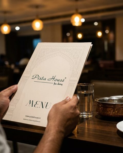 Diner holding the Pista House fine dining menu at a restaurant table with warm pendant lights, photo mockup